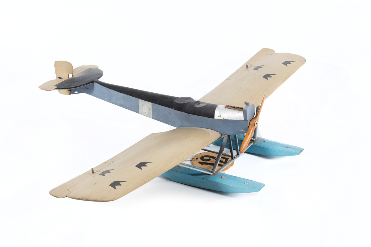 Modell av flygplan, Hansa-Brandenburg. Enmotorigt monoplan, två flottörer. Inbyggd flygkropp, placerad ovan vingarna. Breda och långa vingar med horisontala roder, vars ytterkant skjuta utanför vingarna. Stjärt med halvcirkelformad bäryta, två horisontala roder av oregelbunden form och med vågig akterkant, ett vertikalt roder. Stöttor och stag av metall. Gråmålat. Flygkropp svart- och blåmålad, flottörer blå. Motorhuv försilvrad.