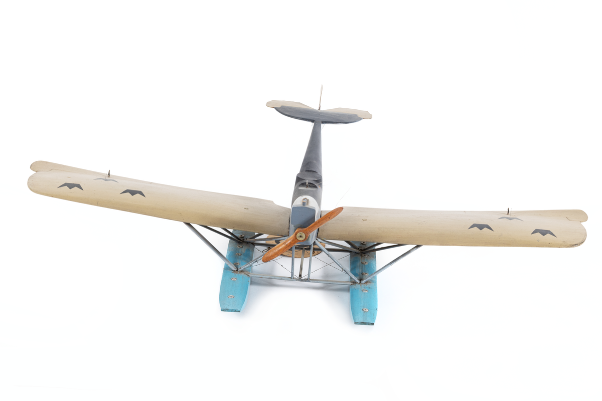 Modell av flygplan, Hansa-Brandenburg. Enmotorigt monoplan, två flottörer. Inbyggd flygkropp, placerad ovan vingarna. Breda och långa vingar med horisontala roder, vars ytterkant skjuta utanför vingarna. Stjärt med halvcirkelformad bäryta, två horisontala roder av oregelbunden form och med vågig akterkant, ett vertikalt roder. Stöttor och stag av metall. Gråmålat. Flygkropp svart- och blåmålad, flottörer blå. Motorhuv försilvrad.