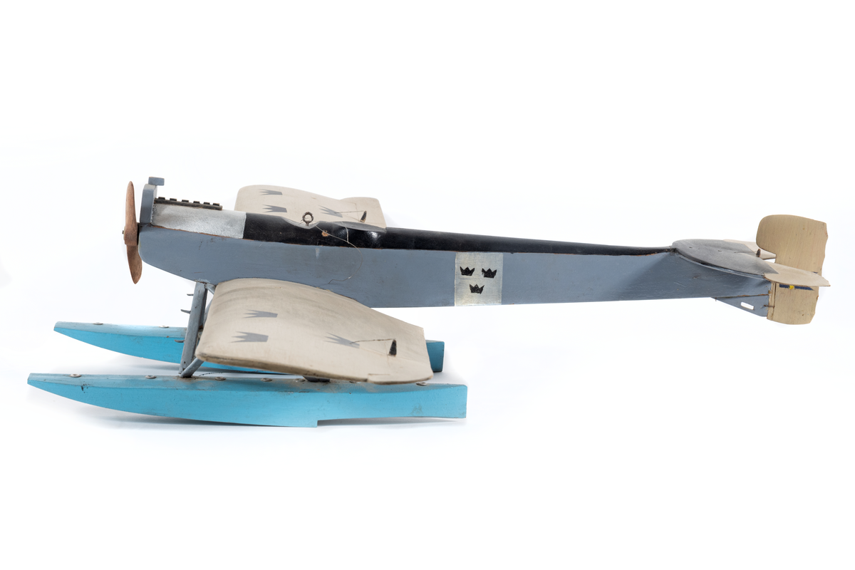 Modell av flygplan, Hansa-Brandenburg. Enmotorigt monoplan, två flottörer. Inbyggd flygkropp, placerad ovan vingarna. Breda och långa vingar med horisontala roder, vars ytterkant skjuta utanför vingarna. Stjärt med halvcirkelformad bäryta, två horisontala roder av oregelbunden form och med vågig akterkant, ett vertikalt roder. Stöttor och stag av metall. Gråmålat. Flygkropp svart- och blåmålad, flottörer blå. Motorhuv försilvrad.