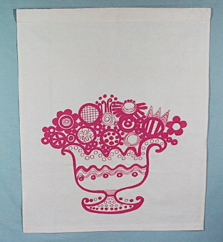 Paradhandduk på ljus linnebotten, broderad med rött bomullsgarn i kraftiga linjer. En stor dekorerad skål på fot fylld med naiva blommor, med ränder, rutor, prickar och cirklar broderade efter 
påritat mönster i kedjesöm, stjälksöm och schattersöm.