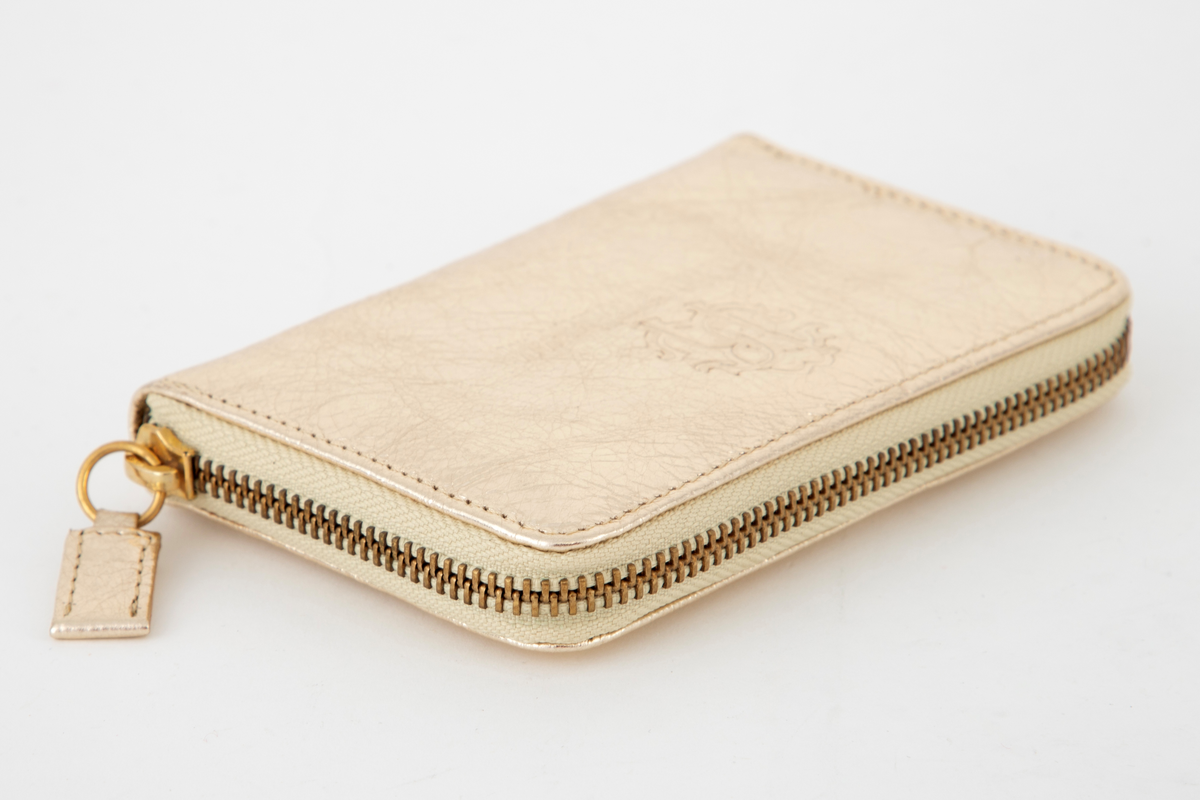 Liten veske, lukket med glidelås og med tre rom. De to hovedrommene har tre lommer hver for kort, mens skilleveggen er et lite glidelåsrom til f. eks. mynter. Innersiden er gullfarget, som yttersiden. Brukes som såkalt clutch, dvs. liten dameveske uten hank.