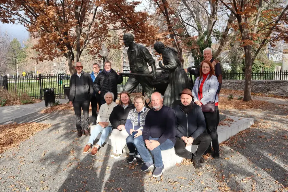 En gruppe mennesker ved en bronsestatue. Trær med brune blader i bakgrunn.