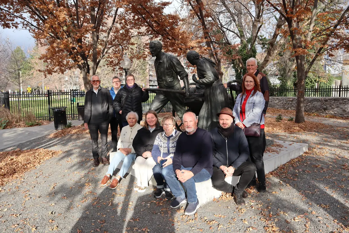 En gruppe mennesker ved en bronsestatue. Trær med brune blader i bakgrunn.