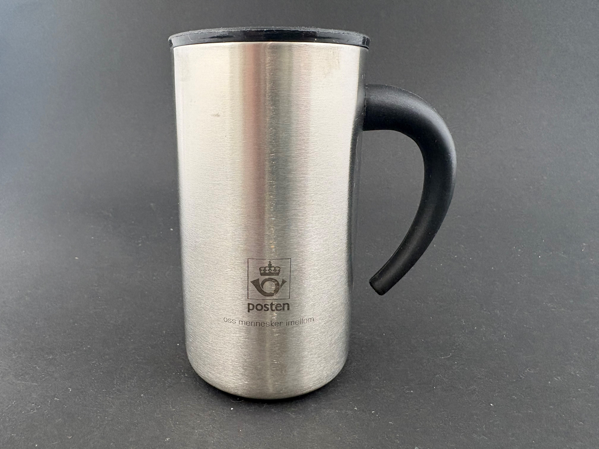 Termokrus. Original eske av kartong. Blankt metall, sort hank og lokk med drikkespalte. Posten-logo over "oss mennesker imellom".