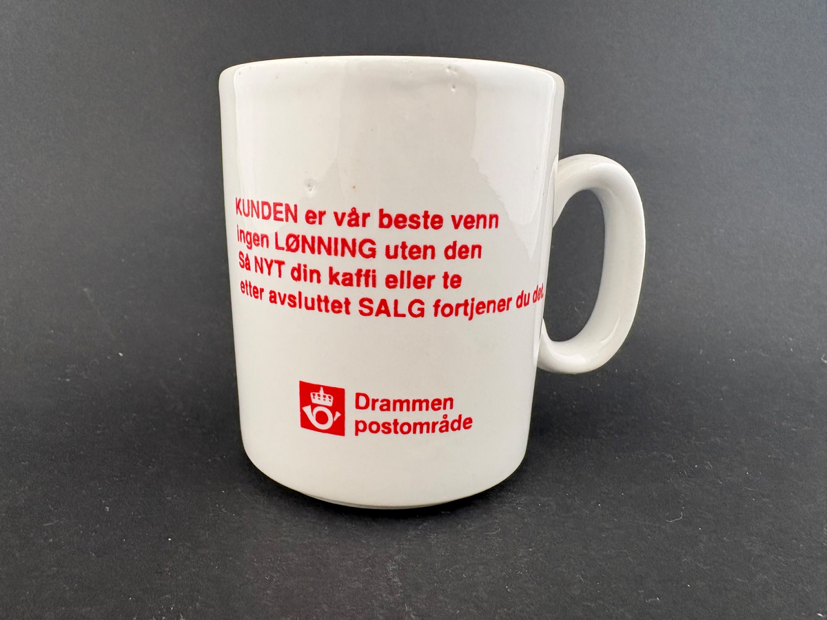 Hvitt krus. Postlogo og "Drammen Postområde" under tekst, alt i rødt. Humoristisk tegning av posthorn med armer, bein og smilende ansikt.