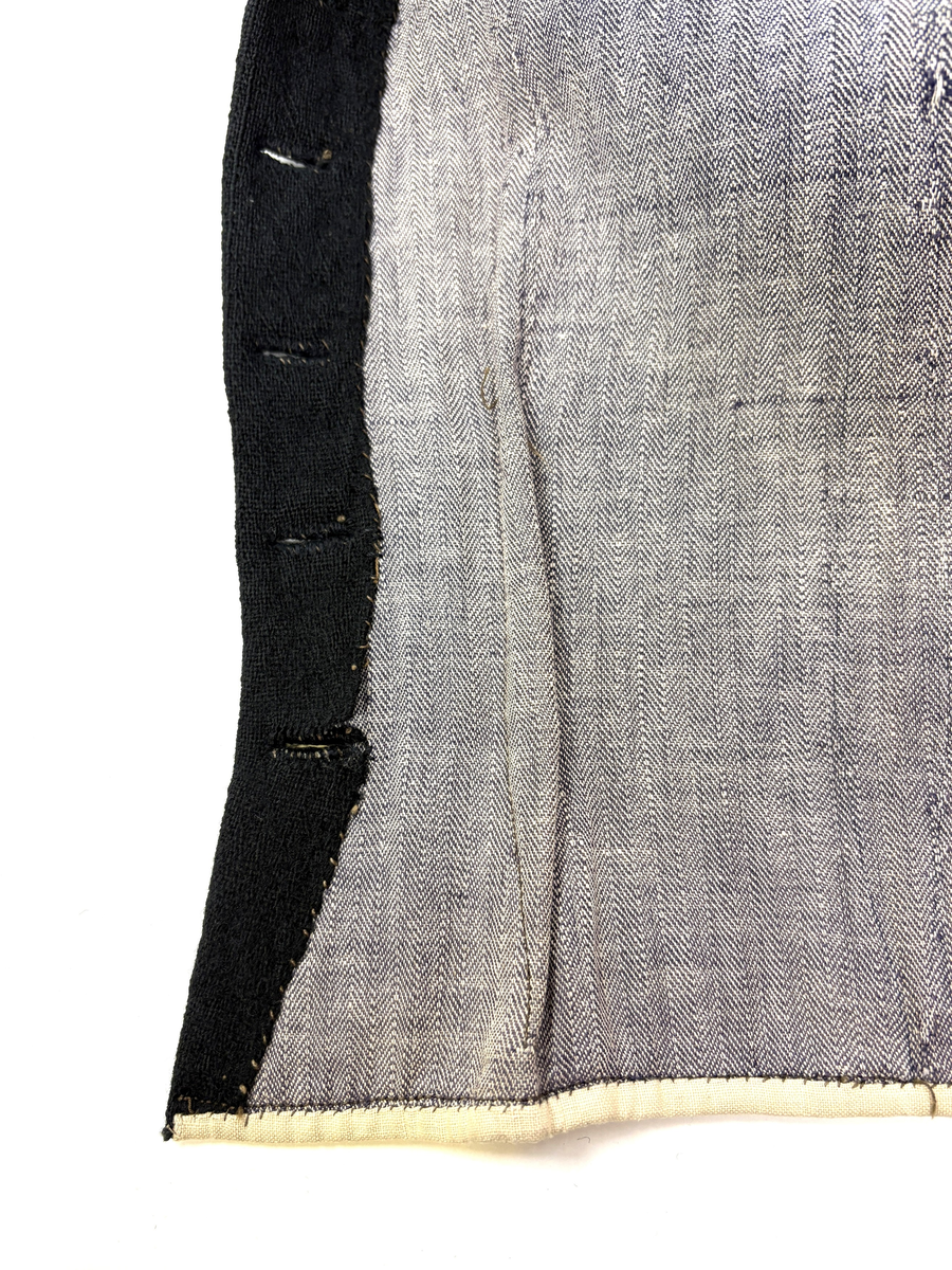 Kjoleliv i svart ull i hjemmevevd toskaft med ermer og bol i samme stoff. Livet er i dag i god stand med noen hull og ellers liten slitasje. Sydd for maskin og hånd med panelsøm og bakovertrekte skuldersømmer og sidesømmer. Rund rigning i halsen og buet fremkant. 2,5 cm bred halslinning i svart kjøpebånd i bomull, sydd på med faldesting og prikkesting med svart bomullstråd. Lukket med 8 svarte kjøpeknapper med preget blomstermønster i horn. Knapphullene er sydd for hånd med svart ulltråd og brun lintråd. Livet har et innsnitt som er 3 cm på det bredeste under bysten, sydd med maskin. Smal tosøms krokarm. Livet er helfôret med ubleket og grå bomull i fiskebensmønster i hjemmevevd toskaft og sydd på samtidig som ullstoffet ble sydd sammen med maskin og spilesøm med tykk bomullstråd for hånd. Nedkanten av livet er kantet med et 0,5 cm bredt ubleket bomullsbånd i hjemmevevd toskaft, sydd på med maskin, lagt over og festet med faldesting for hånd med brun bomullstråd. Midt på bak har livet en 5 cm lang splitt, også kantet med bomullsbåndet. Livet brukes ned i stakken og har en påsydd metallkrok bak til å hekte stakken på.