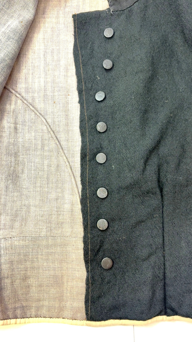 Kjoleliv i svart ull i hjemmevevd toskaft med ermer og bol i samme stoff. Livet er i dag i god stand med noen hull og ellers liten slitasje. Sydd for maskin og hånd med panelsøm og bakovertrekte skuldersømmer og sidesømmer. Rund rigning i halsen og buet fremkant. 2,5 cm bred halslinning i svart kjøpebånd i bomull, sydd på med faldesting og prikkesting med svart bomullstråd. Lukket med 8 svarte kjøpeknapper med preget blomstermønster i horn. Knapphullene er sydd for hånd med svart ulltråd og brun lintråd. Livet har et innsnitt som er 3 cm på det bredeste under bysten, sydd med maskin. Smal tosøms krokarm. Livet er helfôret med ubleket og grå bomull i fiskebensmønster i hjemmevevd toskaft og sydd på samtidig som ullstoffet ble sydd sammen med maskin og spilesøm med tykk bomullstråd for hånd. Nedkanten av livet er kantet med et 0,5 cm bredt ubleket bomullsbånd i hjemmevevd toskaft, sydd på med maskin, lagt over og festet med faldesting for hånd med brun bomullstråd. Midt på bak har livet en 5 cm lang splitt, også kantet med bomullsbåndet. Livet brukes ned i stakken og har en påsydd metallkrok bak til å hekte stakken på.