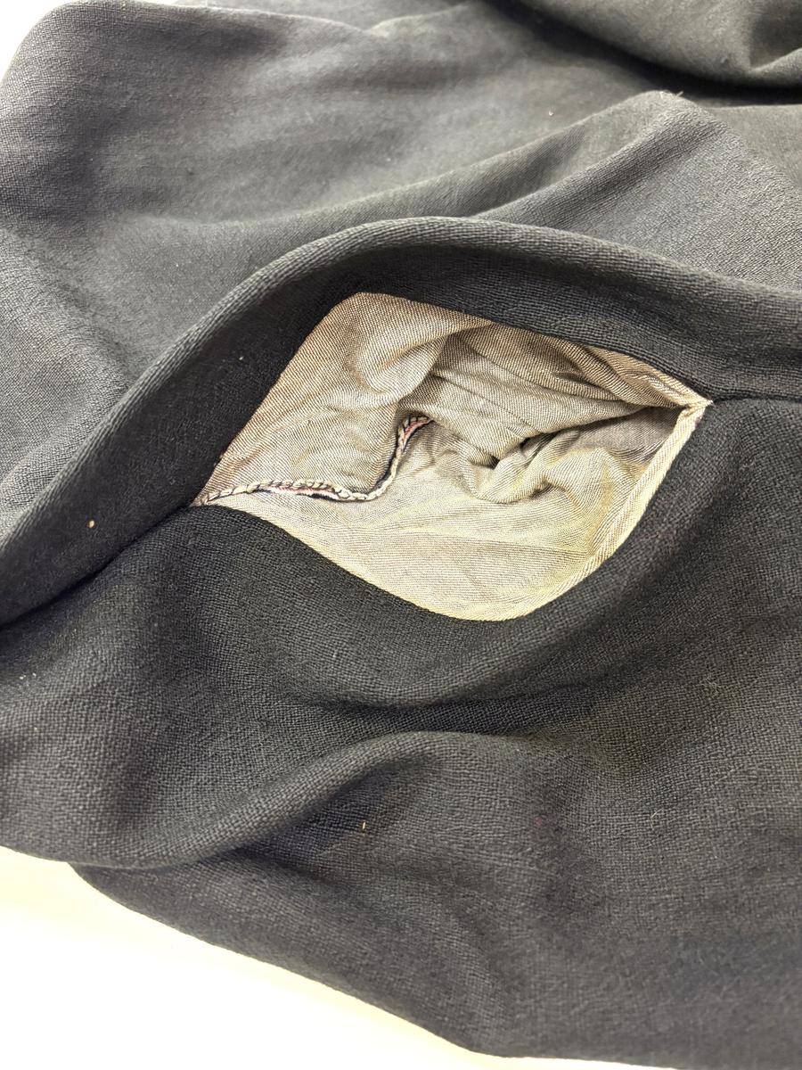 Stakk i samme stoff som liv SM.008024.01; svart ull i hjemmevevd toskaft. Stakken er i god stand med litt slitasje på et pyntebånd. Sydd sammen med maskin med brun bomullstråd av fem vevhøyder med jarekanter. Stakken har et 24 cm bredt glatt stykke midt på foran og foldelagt på begge sider. Åpningen er i venstre side og er 26, 5 cm lang. Stakken har seks folder foldelagt mot høyre og seks folder foldelagt mot venstre, 4-4,5 cm brede. Midt på bak er det et 7,5 cm bredt rynket felt med en halv fold over på begge sider. Foldene er tråklet, sydd på med attersting og så kastet med faldesting med brun bomullstråd. Linningen er i samme stoff som kjolen og 3 cm bred, sydd med faldesting med brun bomullstråd og deretter med prikkesting midt på linningen med samme tråd. Lukkes med to metallhekter. Stakken har en 3 cm bred hengefald 10 cm fra nedkanten, sydd med faldesting med brun bomullstråd. Pyntet nede med to fløyelsbånd som er 0,7 og 1 cm brede, sydd på for hånd i øverste kant av båndet med prikkesting med svart bomullstråd. 0,5 cm bred kostekant i fløyel sydd på med atter- og faldesting for hånd med attersting med svart bomullstråd. Stakken har en 24 cm lang og 17 cm bred lomme på høyre side i samme stoff som fôret på livet, sydd med attersting med svart bomullstråd og festet til stakken med maskin med brun bomullstråd. Stakken har en metallhempe midt på bak på linningen for å henge på livet, og stakken skal brukes ned i livet.