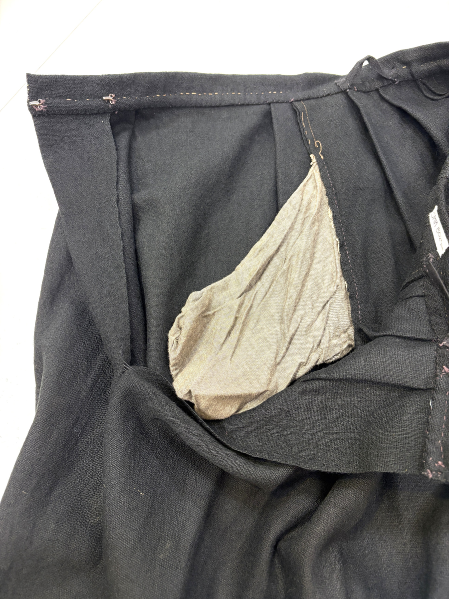 Stakk i samme stoff som liv SM.008024.01; svart ull i hjemmevevd toskaft. Stakken er i god stand med litt slitasje på et pyntebånd. Sydd sammen med maskin med brun bomullstråd av fem vevhøyder med jarekanter. Stakken har et 24 cm bredt glatt stykke midt på foran og foldelagt på begge sider. Åpningen er i venstre side og er 26, 5 cm lang. Stakken har seks folder foldelagt mot høyre og seks folder foldelagt mot venstre, 4-4,5 cm brede. Midt på bak er det et 7,5 cm bredt rynket felt med en halv fold over på begge sider. Foldene er tråklet, sydd på med attersting og så kastet med faldesting med brun bomullstråd. Linningen er i samme stoff som kjolen og 3 cm bred, sydd med faldesting med brun bomullstråd og deretter med prikkesting midt på linningen med samme tråd. Lukkes med to metallhekter. Stakken har en 3 cm bred hengefald 10 cm fra nedkanten, sydd med faldesting med brun bomullstråd. Pyntet nede med to fløyelsbånd som er 0,7 og 1 cm brede, sydd på for hånd i øverste kant av båndet med prikkesting med svart bomullstråd. 0,5 cm bred kostekant i fløyel sydd på med atter- og faldesting for hånd med attersting med svart bomullstråd. Stakken har en 24 cm lang og 17 cm bred lomme på høyre side i samme stoff som fôret på livet, sydd med attersting med svart bomullstråd og festet til stakken med maskin med brun bomullstråd. Stakken har en metallhempe midt på bak på linningen for å henge på livet, og stakken skal brukes ned i livet.