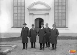 Fem Herrar varav en prästklädd med doktorshattI mitten står 