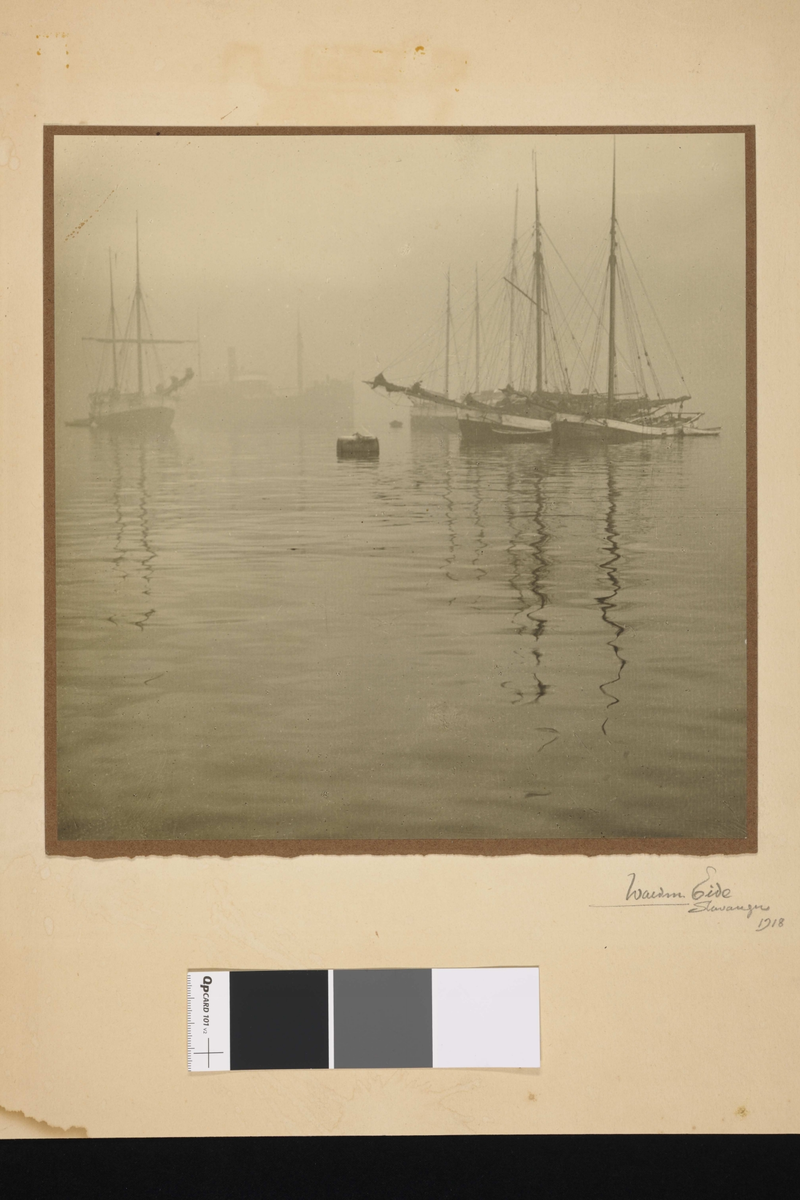 Båter i havnen med seilmaster som speiler seg i vannet.