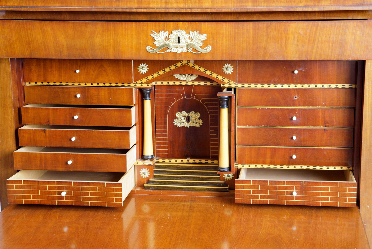 Chiffonje av mahogny. Fanerat och med intarsia på den inre inredningen. Utförd med speciell inredning med flera lönnfack. Lådorna och klaffen har förgyllda beslag. Har varit brukad för förvaring.
Inskriven i huvudkatalog 1943.