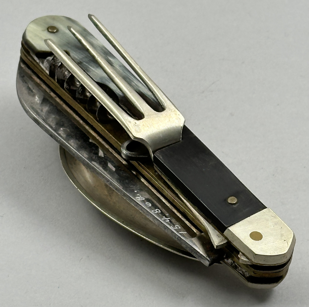 Bestick, fällkniv med handtag av horn och knivblad av stål, sked och gaffel av försilvrad metall, samt dessutom korkskruv och handskknäppare. Signerad: '59 Sauvagnat'.