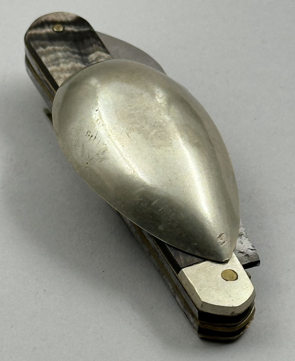 Bestick, fällkniv med handtag av horn och knivblad av stål, sked och gaffel av försilvrad metall, samt dessutom korkskruv och handskknäppare. Signerad: '59 Sauvagnat'.