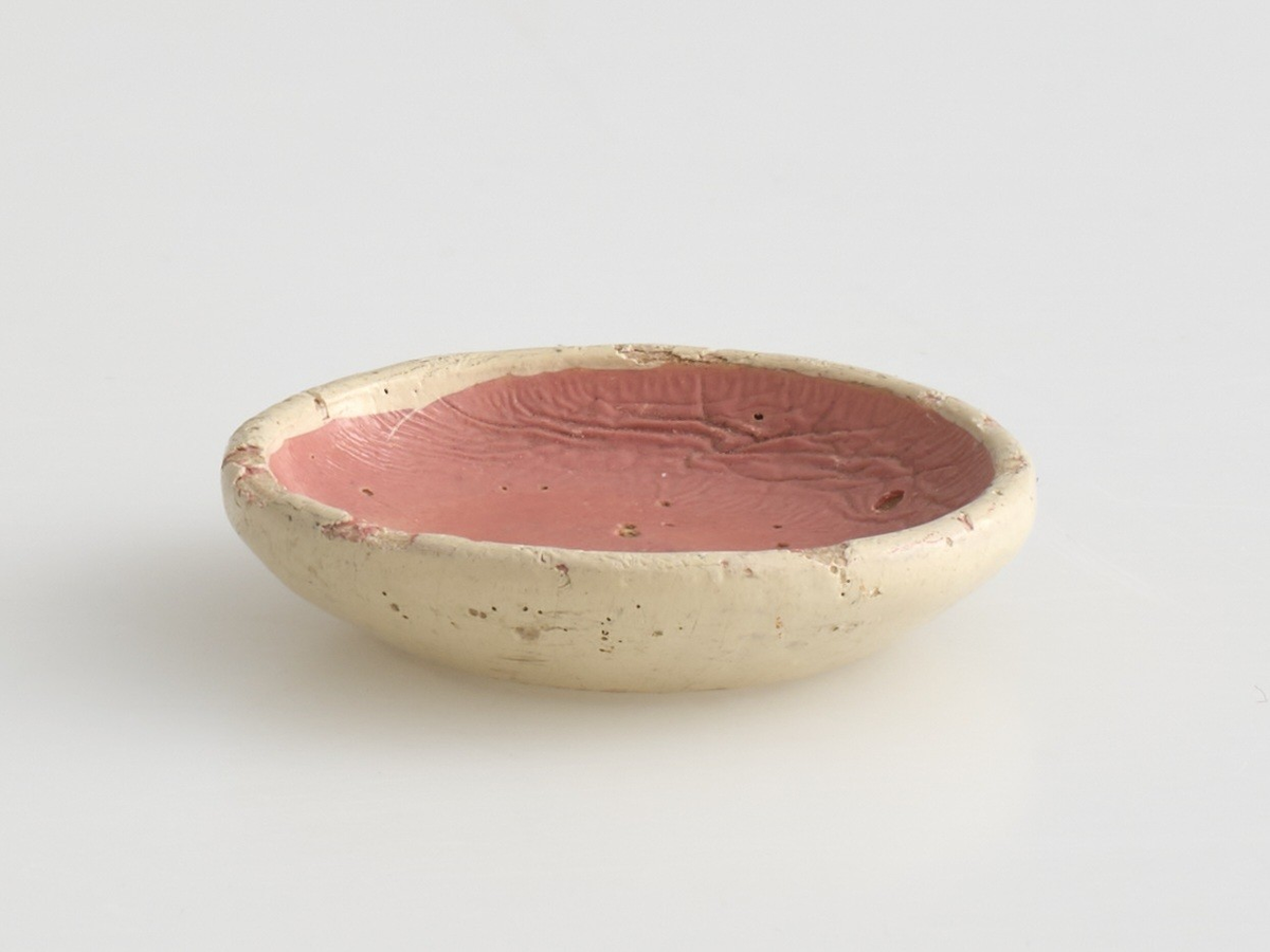 Serveringssett i miniatyr, lagd av tre.
Settet består av en tallerken, en kopp, en mugge og en krukke. Hele settet er malt i samme farger dekorert med likt mønster, utenom tallerkenen som ikke har malt mønster.
Tallerkenen har forhøyet kanter, og er malt rosa på innsiden, med hvite kanter og hvit underside.
Koppen er malt hvit på innsiden, og har en svartmalt hank. Hanken er øreformet og er festet fra kanten øverst til hvor koppen buer seg innover ved foten. Utsiden av koppen er malt rosa, og dekorert med blåe streker som danner trekanter med ujevne linjer rundt koppen. På toppen av trekantene er det malt en rød sirkel.
Krukken er sylinder-formet og snevres inn i mot toppen, før den vies skrått utover rundt åpningen. Krukken er malt hvit på innsiden, og rosa på utsiden, utsiden er også dekorert med samme mønster som koppen. Kanten rundt krukkens åpning er delvis brukket av.
Muggen er sylindret-formet, og snevres inn mot toppen, hvor kanten rundt åpningen forhøyes mot helletuten på den ene siden. På motsatt side av helletuten er det festet en svart-malt hank. Oversiden av hanken er rett, og bues ned mot bunnen av muggen. Muggen er malt og dekorert likt som koppen.