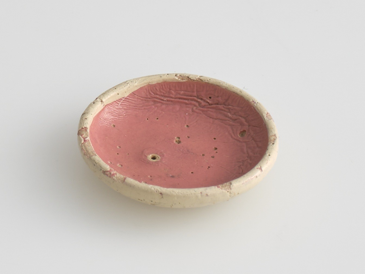 Serveringssett i miniatyr, lagd av tre.
Settet består av en tallerken, en kopp, en mugge og en krukke. Hele settet er malt i samme farger dekorert med likt mønster, utenom tallerkenen som ikke har malt mønster.
Tallerkenen har forhøyet kanter, og er malt rosa på innsiden, med hvite kanter og hvit underside.
Koppen er malt hvit på innsiden, og har en svartmalt hank. Hanken er øreformet og er festet fra kanten øverst til hvor koppen buer seg innover ved foten. Utsiden av koppen er malt rosa, og dekorert med blåe streker som danner trekanter med ujevne linjer rundt koppen. På toppen av trekantene er det malt en rød sirkel.
Krukken er sylinder-formet og snevres inn i mot toppen, før den vies skrått utover rundt åpningen. Krukken er malt hvit på innsiden, og rosa på utsiden, utsiden er også dekorert med samme mønster som koppen. Kanten rundt krukkens åpning er delvis brukket av.
Muggen er sylindret-formet, og snevres inn mot toppen, hvor kanten rundt åpningen forhøyes mot helletuten på den ene siden. På motsatt side av helletuten er det festet en svart-malt hank. Oversiden av hanken er rett, og bues ned mot bunnen av muggen. Muggen er malt og dekorert likt som koppen.