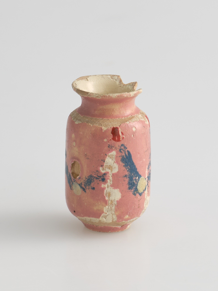 Serveringssett i miniatyr, lagd av tre.
Settet består av en tallerken, en kopp, en mugge og en krukke. Hele settet er malt i samme farger dekorert med likt mønster, utenom tallerkenen som ikke har malt mønster.
Tallerkenen har forhøyet kanter, og er malt rosa på innsiden, med hvite kanter og hvit underside.
Koppen er malt hvit på innsiden, og har en svartmalt hank. Hanken er øreformet og er festet fra kanten øverst til hvor koppen buer seg innover ved foten. Utsiden av koppen er malt rosa, og dekorert med blåe streker som danner trekanter med ujevne linjer rundt koppen. På toppen av trekantene er det malt en rød sirkel.
Krukken er sylinder-formet og snevres inn i mot toppen, før den vies skrått utover rundt åpningen. Krukken er malt hvit på innsiden, og rosa på utsiden, utsiden er også dekorert med samme mønster som koppen. Kanten rundt krukkens åpning er delvis brukket av.
Muggen er sylindret-formet, og snevres inn mot toppen, hvor kanten rundt åpningen forhøyes mot helletuten på den ene siden. På motsatt side av helletuten er det festet en svart-malt hank. Oversiden av hanken er rett, og bues ned mot bunnen av muggen. Muggen er malt og dekorert likt som koppen.