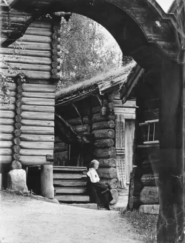 Lillehammer. Maihaugen. Bunadkledd jente sitter på stabburstrappa på Bjørnstad.