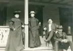 En okänd kvinna tillsammans med fru Elisabeth Bergstedt, landsfiskal Filip Rehnström och kronolänsman Albert Bergstedt på en verandatrappa.
Kvinnorna är klädda i långa s.k. bilkappor (som också kunde användas vid regnväder, vilket ena kvinnans paraply indikerar).
Trol. foto från dåv. restaurangen på Evedal, Växjö.