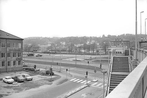 Fotografi som är taget från den då nya gjutna motorbron, kallad Mölndals bro.

Fotot är taget någon gång i början av 1970-talet. Två vuxna människor som har ryggarna vända åt fotografen; går på trottoaren, runt hörnet av Hantverkshuset, till vänster i bild.

I bakgrunden till höger ses huset Röda kvarn eller Moulin Rouge. Dessutom syns i bakgrunden till vänster järnvägsstationen Mölndals Nedre. Långt i bakgrunden i mitten skymtar brandstationen på Torggatan 2 och 4 och snett bakom denna finns Missionskyrkan i stadsdelen Trädgården.

Till vänster närmast i bild, på en tegelhusvägg, ses en skylt för bankverksamhet, inrymt i det så kallade Hantverkshuset.