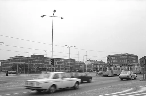Fotografiet visar en vy som visar stadshuset och på avstånd platsen där Mölndals stadsbibliotek och Folkets hus ligger samlade.
Människor går på trottoarer och personbilar kör i riktningar både till och från Göteborg.

Mölndals Taxistation, med adressen Tempelgatan 2, syns om man tittar riktigt noga, nära belägen till vänster om stadshuset på fotografiet.

En spårvagn far in mot Göteborg.