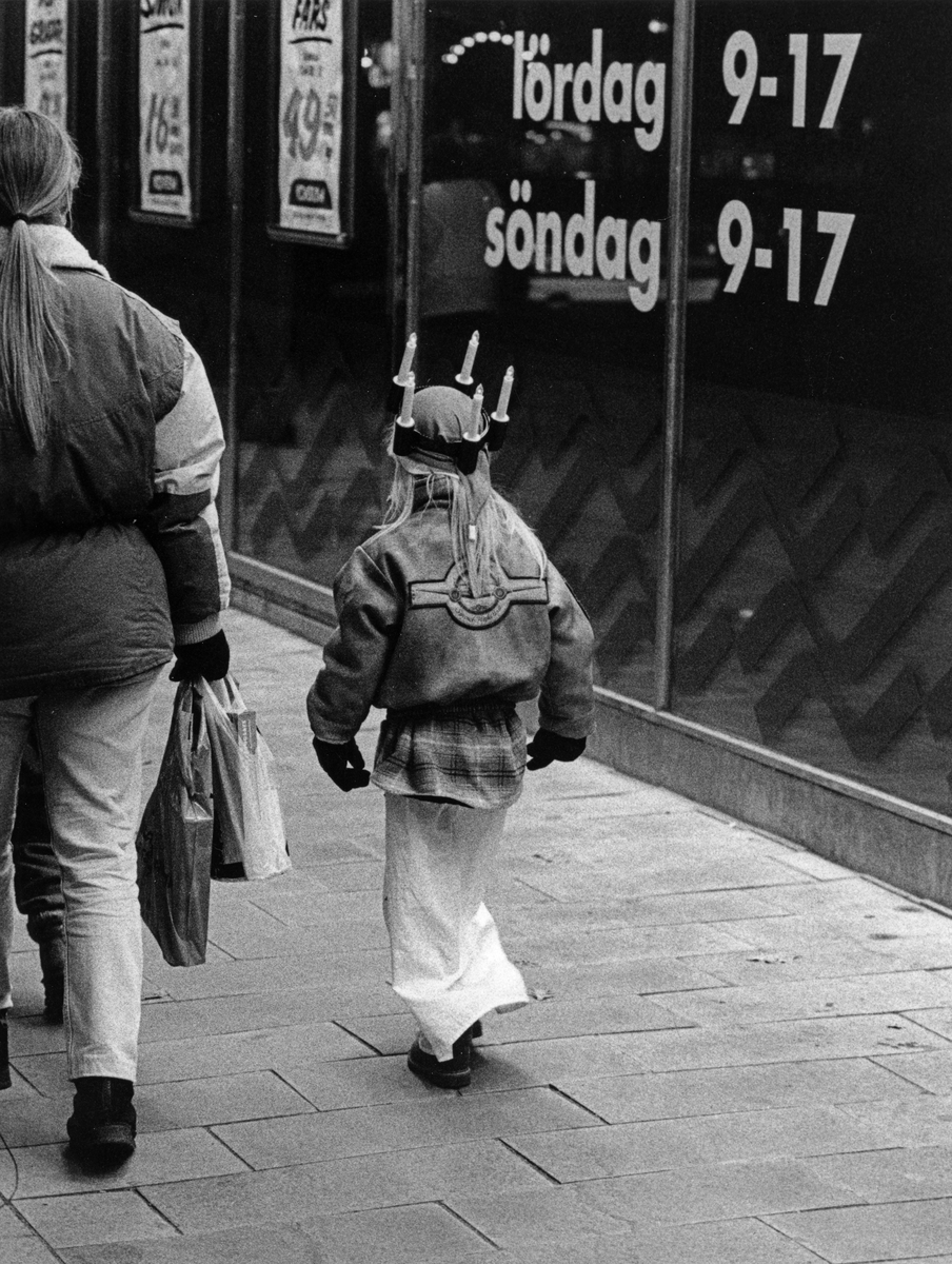 En flicka med lucianattlinne, ytterjacka och en luciakrona med batteriljus går på Centralgatan vid Konsum. 