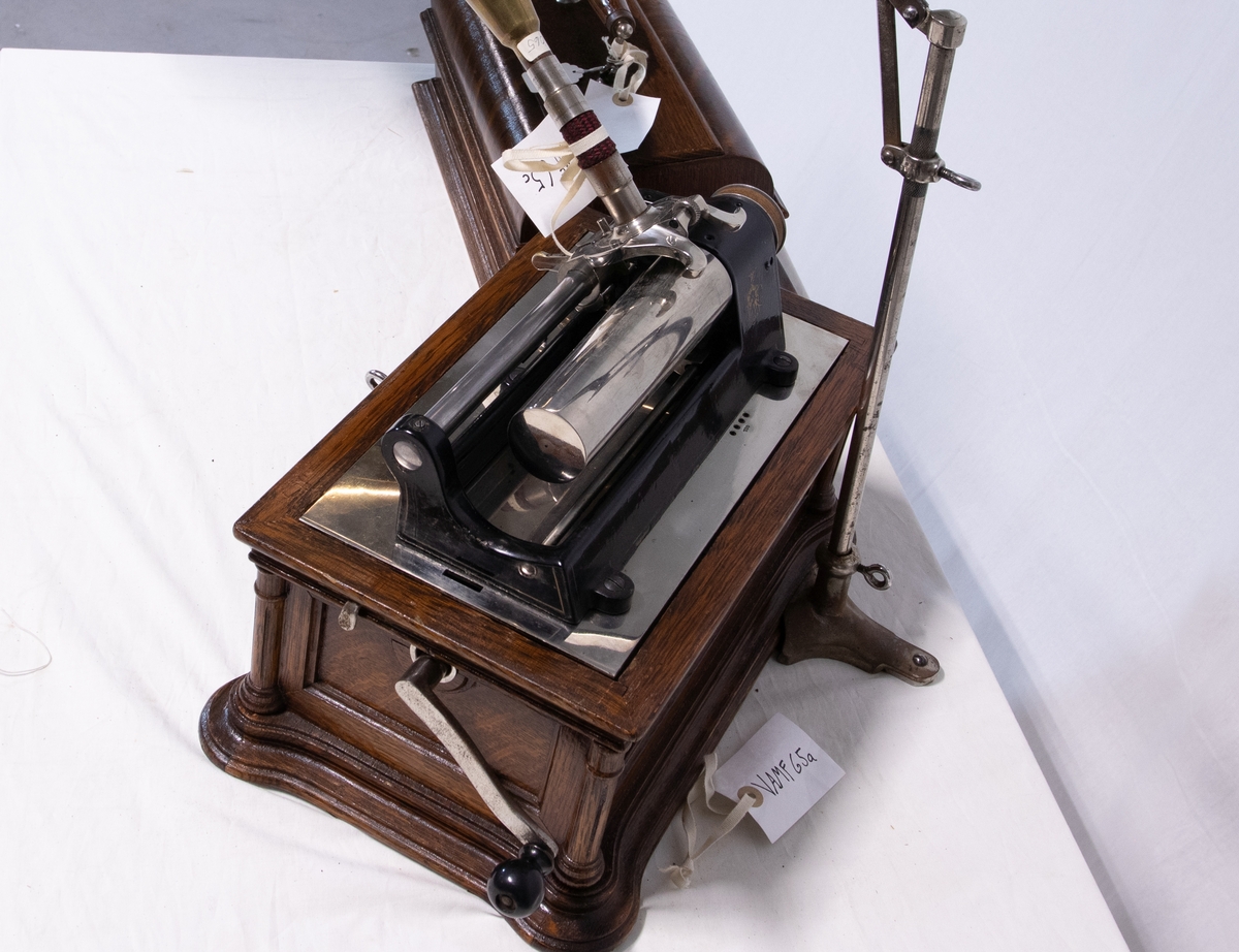 Sveivefonograf. Comlumbia Graphophone modell BF, også kalt "Peerless", nr. 7644. Fonografen er laget for av- og innspilling av 2- og 3 minutters sylindere. Avspillingslydhodet er en "Lyric" nr. 55735. Innspillingslydhodet er uten nr. og navn. Motoren er sveivetrukket med 4 fjærer.

Kassen er i brun eik med buet avtagbart lokk. Kassen er dekorert med utskjærte søyler i hjørnen. På baksiden av kassen er det montert et opphengsstativ til et stort messinghorn.