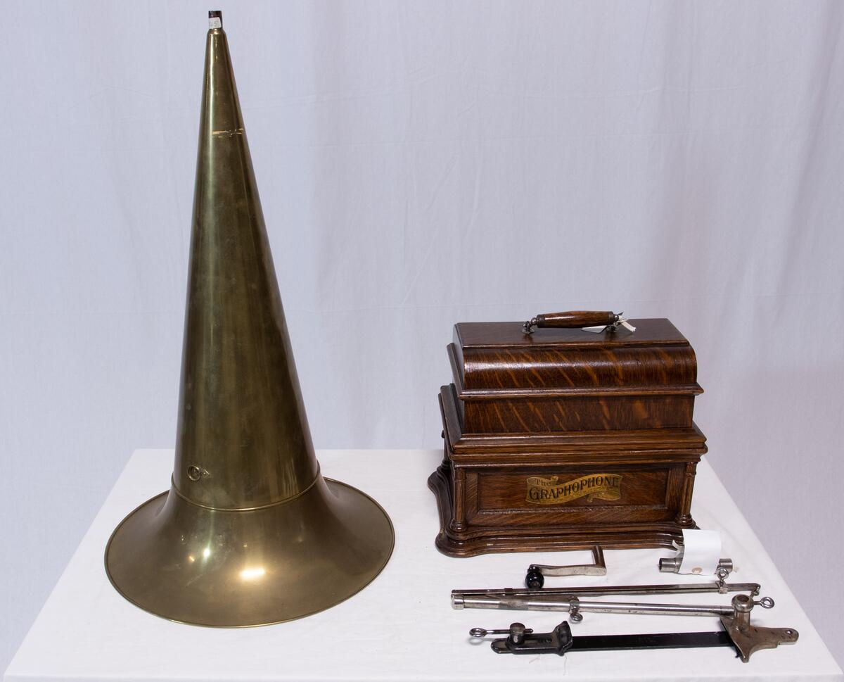 Sveivefonograf. Comlumbia Graphophone modell BF, også kalt "Peerless", nr. 7644. Fonografen er laget for av- og innspilling av 2- og 3 minutters sylindere. Avspillingslydhodet er en "Lyric" nr. 55735. Innspillingslydhodet er uten nr. og navn. Motoren er sveivetrukket med 4 fjærer.

Kassen er i brun eik med buet avtagbart lokk. Kassen er dekorert med utskjærte søyler i hjørnen. På baksiden av kassen er det montert et opphengsstativ til et stort messinghorn.