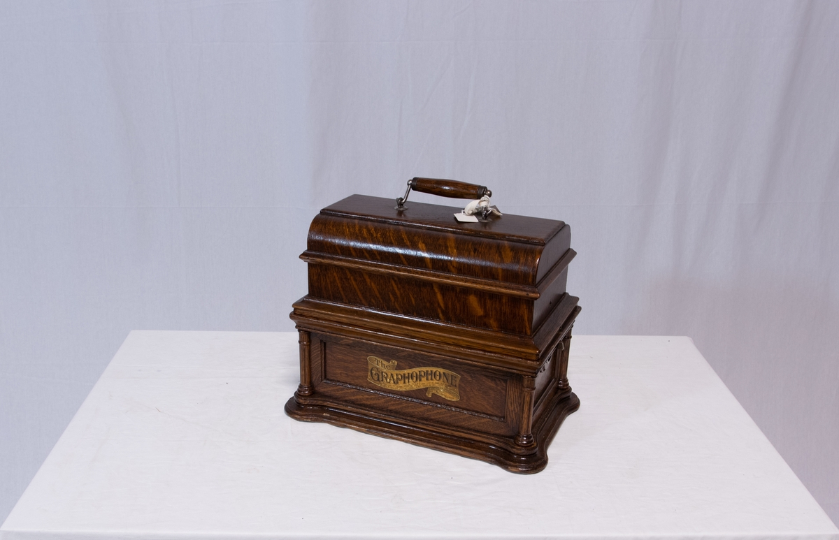 Sveivefonograf. Comlumbia Graphophone modell BF, også kalt "Peerless", nr. 7644. Fonografen er laget for av- og innspilling av 2- og 3 minutters sylindere. Avspillingslydhodet er en "Lyric" nr. 55735. Innspillingslydhodet er uten nr. og navn. Motoren er sveivetrukket med 4 fjærer.

Kassen er i brun eik med buet avtagbart lokk. Kassen er dekorert med utskjærte søyler i hjørnen. På baksiden av kassen er det montert et opphengsstativ til et stort messinghorn.