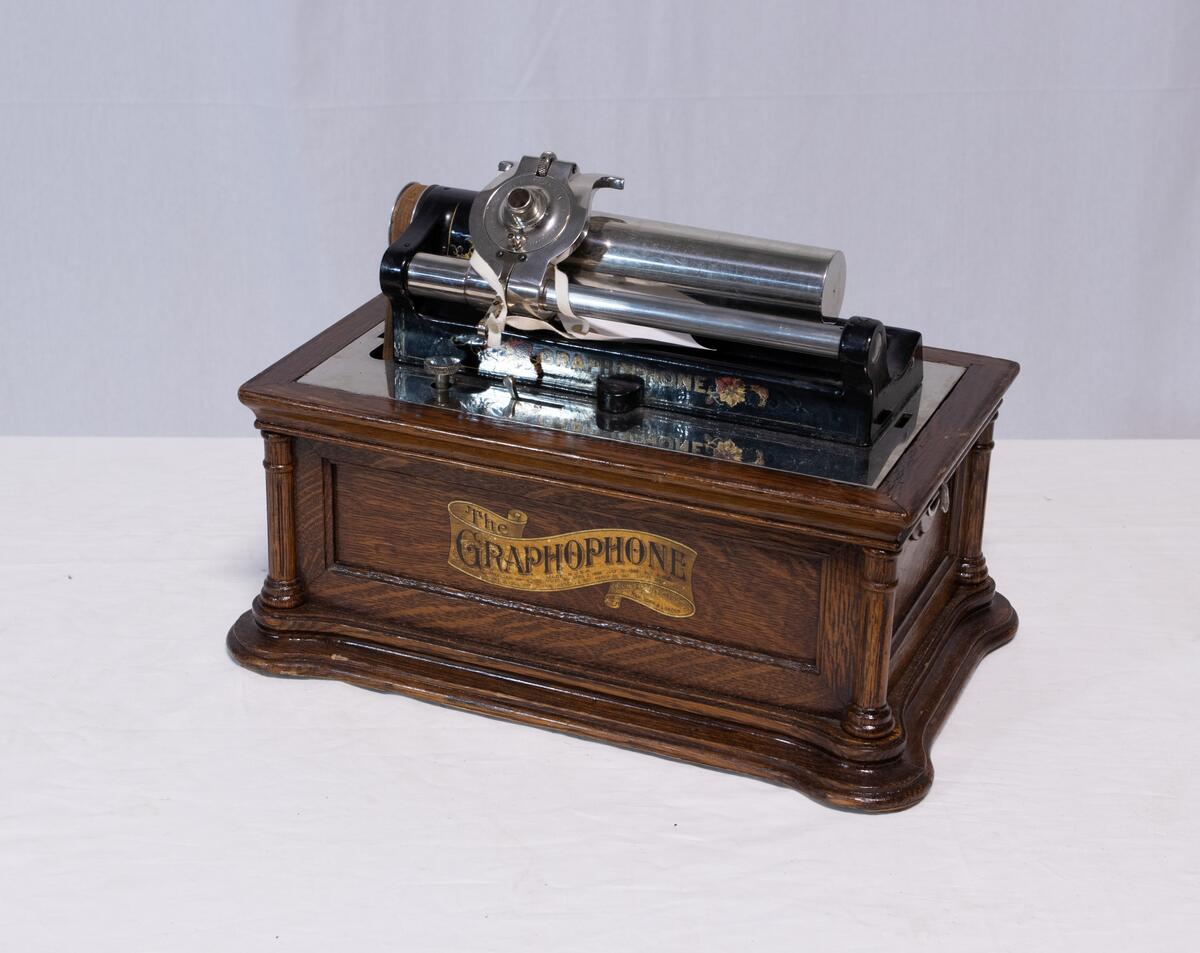 Sveivefonograf. Comlumbia Graphophone modell BF, også kalt "Peerless", nr. 7644. Fonografen er laget for av- og innspilling av 2- og 3 minutters sylindere. Avspillingslydhodet er en "Lyric" nr. 55735. Innspillingslydhodet er uten nr. og navn. Motoren er sveivetrukket med 4 fjærer.

Kassen er i brun eik med buet avtagbart lokk. Kassen er dekorert med utskjærte søyler i hjørnen. På baksiden av kassen er det montert et opphengsstativ til et stort messinghorn.