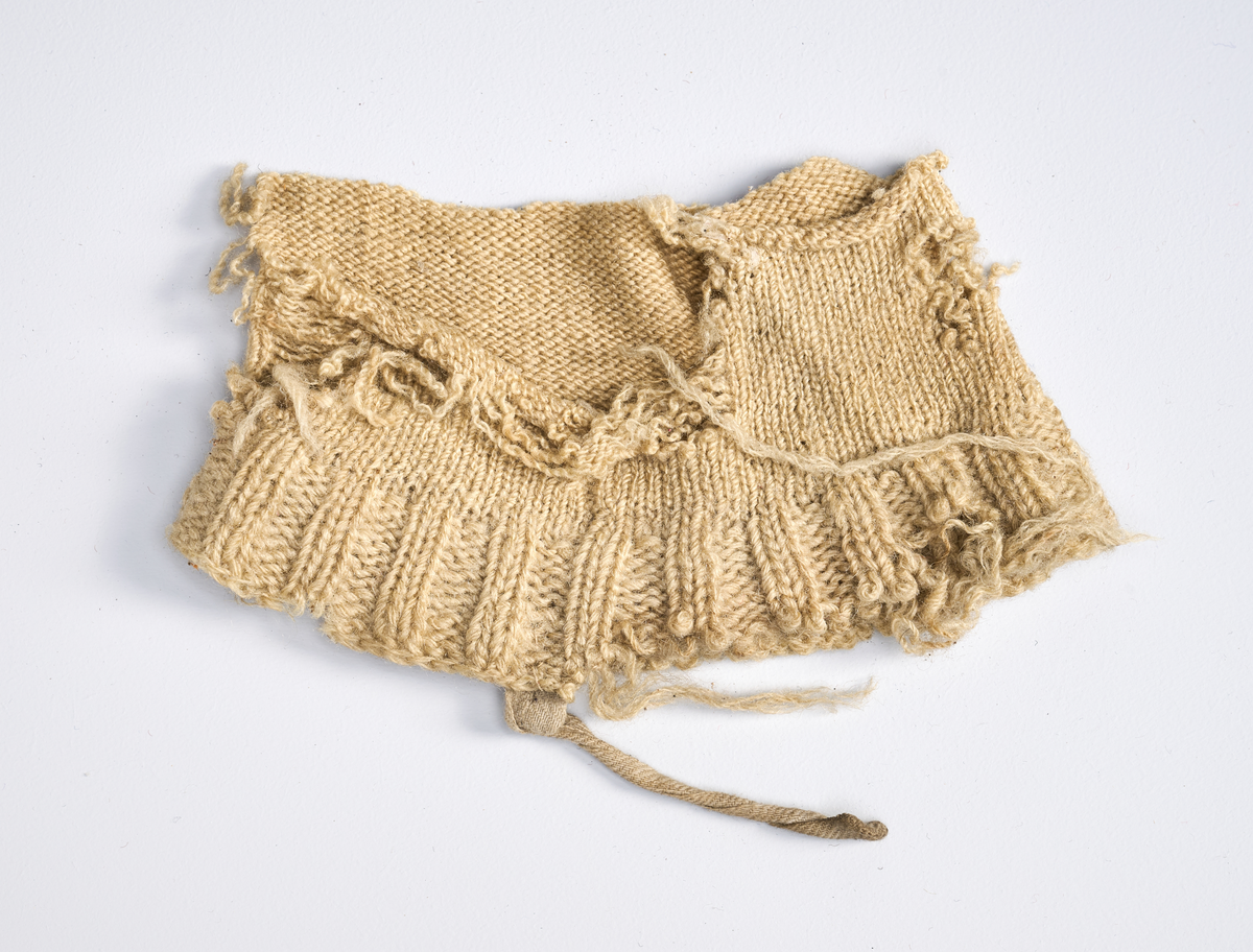 Ulike strikkete stoffrester i ulike farger og mønster. Et stoff er et brodert stoltrekk med blomstermønster. Funnet i en kasse tilhørende Hans Nissengården.