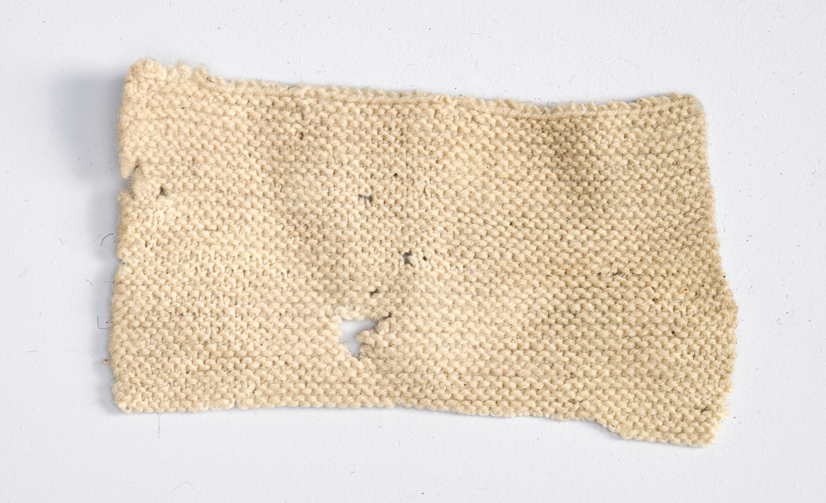 Ulike strikkete stoffrester i ulike farger og mønster. Et stoff er et brodert stoltrekk med blomstermønster. Funnet i en kasse tilhørende Hans Nissengården.