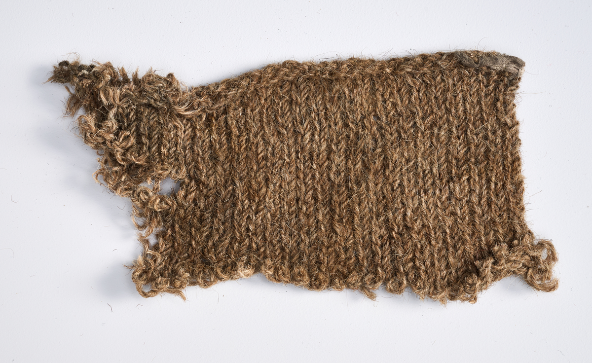 Ulike strikkete stoffrester i ulike farger og mønster. Et stoff er et brodert stoltrekk med blomstermønster. Funnet i en kasse tilhørende Hans Nissengården.