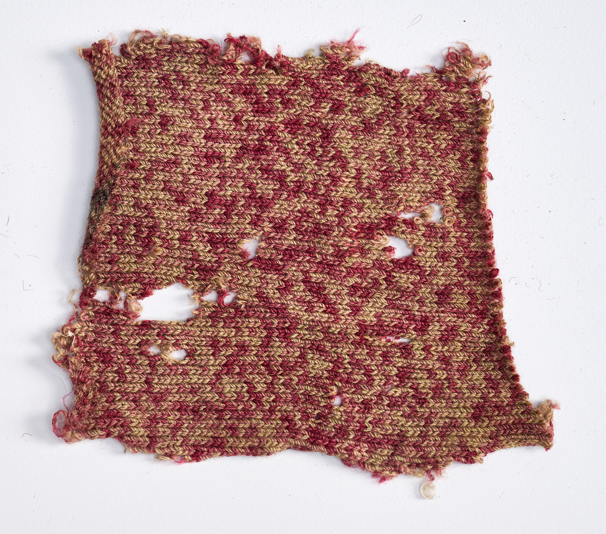 Ulike strikkete stoffrester i ulike farger og mønster. Et stoff er et brodert stoltrekk med blomstermønster. Funnet i en kasse tilhørende Hans Nissengården.