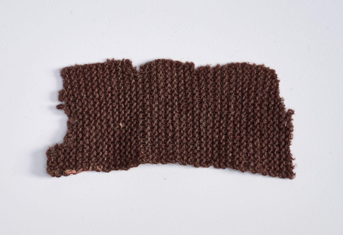 Ulike strikkete stoffrester i ulike farger og mønster. Et stoff er et brodert stoltrekk med blomstermønster. Funnet i en kasse tilhørende Hans Nissengården.