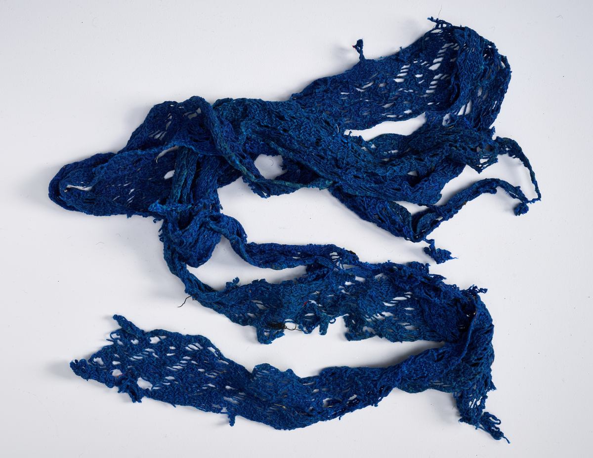 Ulike strikkete stoffrester i ulike farger og mønster. Et stoff er et brodert stoltrekk med blomstermønster. Funnet i en kasse tilhørende Hans Nissengården.