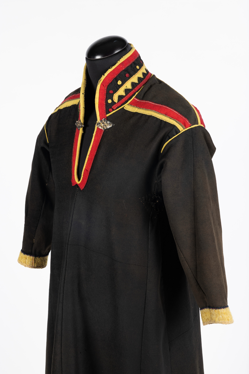 Svart kofte av klede med dekor av gult, rødt og beige klede.