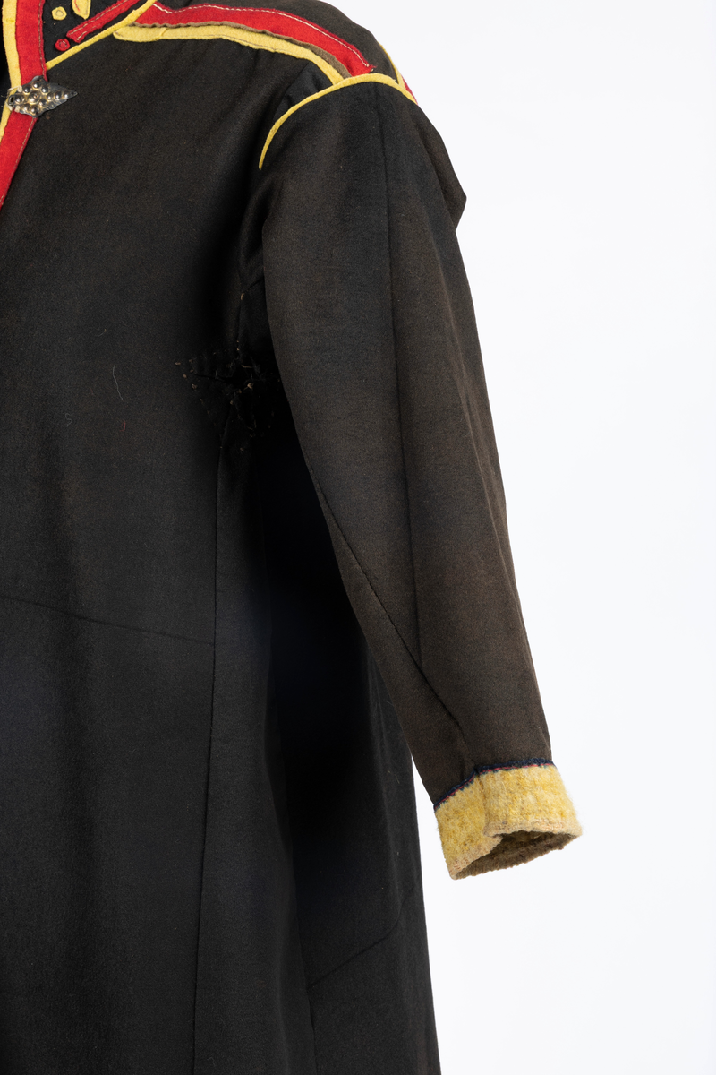 Svart kofte av klede med dekor av gult, rødt og beige klede.