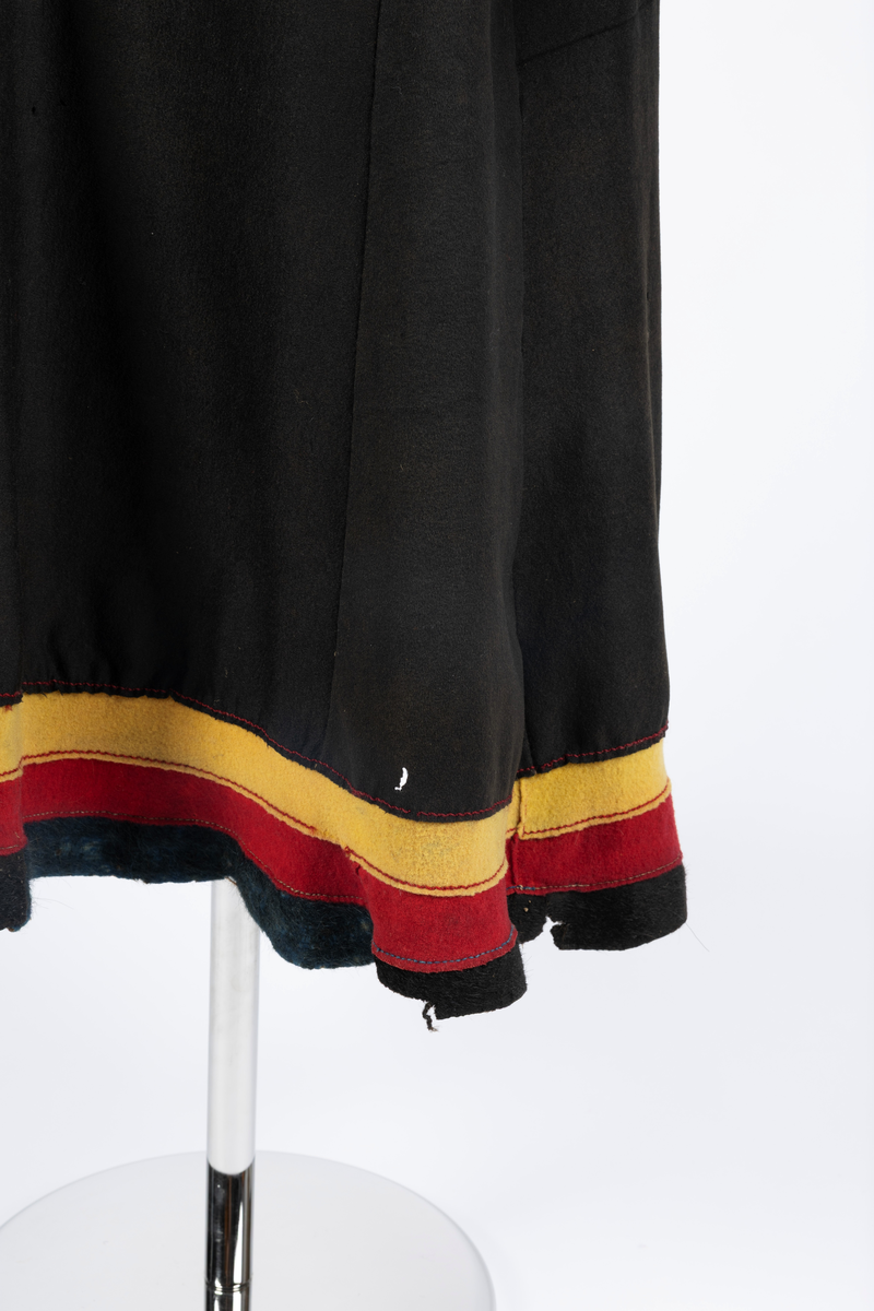 Svart kofte av klede med dekor av gult, rødt og beige klede.