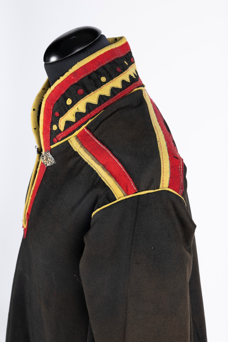 Svart kofte av klede med dekor av gult, rødt og beige klede.