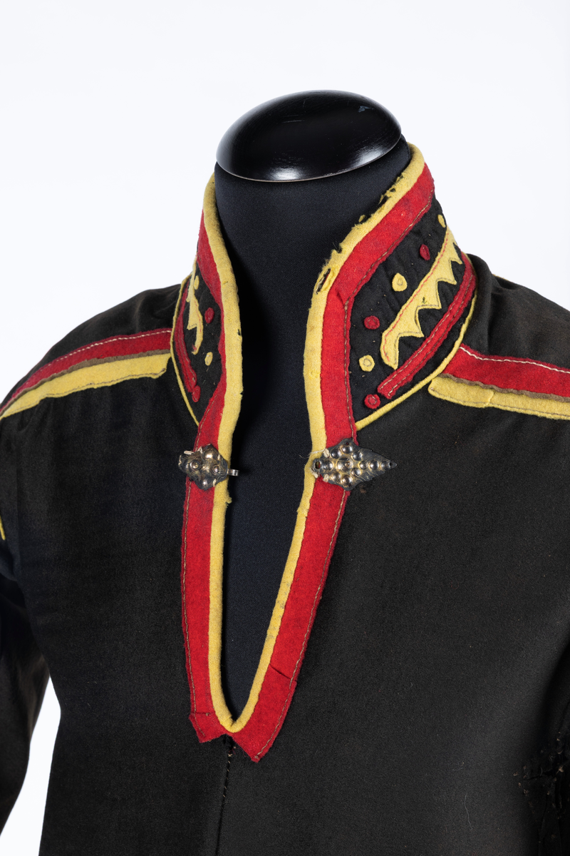 Svart kofte av klede med dekor av gult, rødt og beige klede.