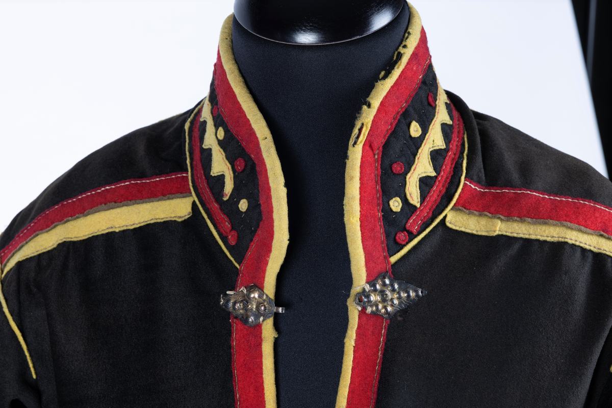 Svart kofte av klede med dekor av gult, rødt og beige klede.