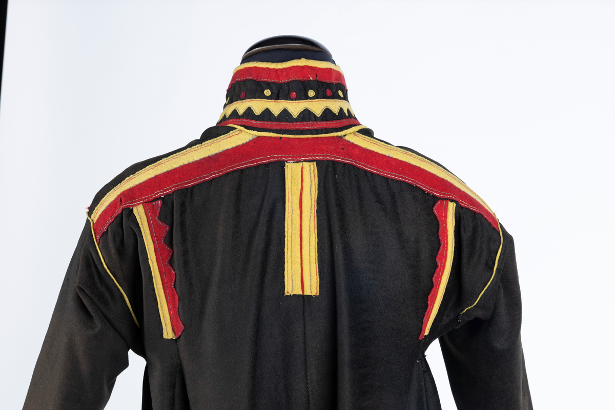 Svart kofte av klede med dekor av gult, rødt og beige klede.