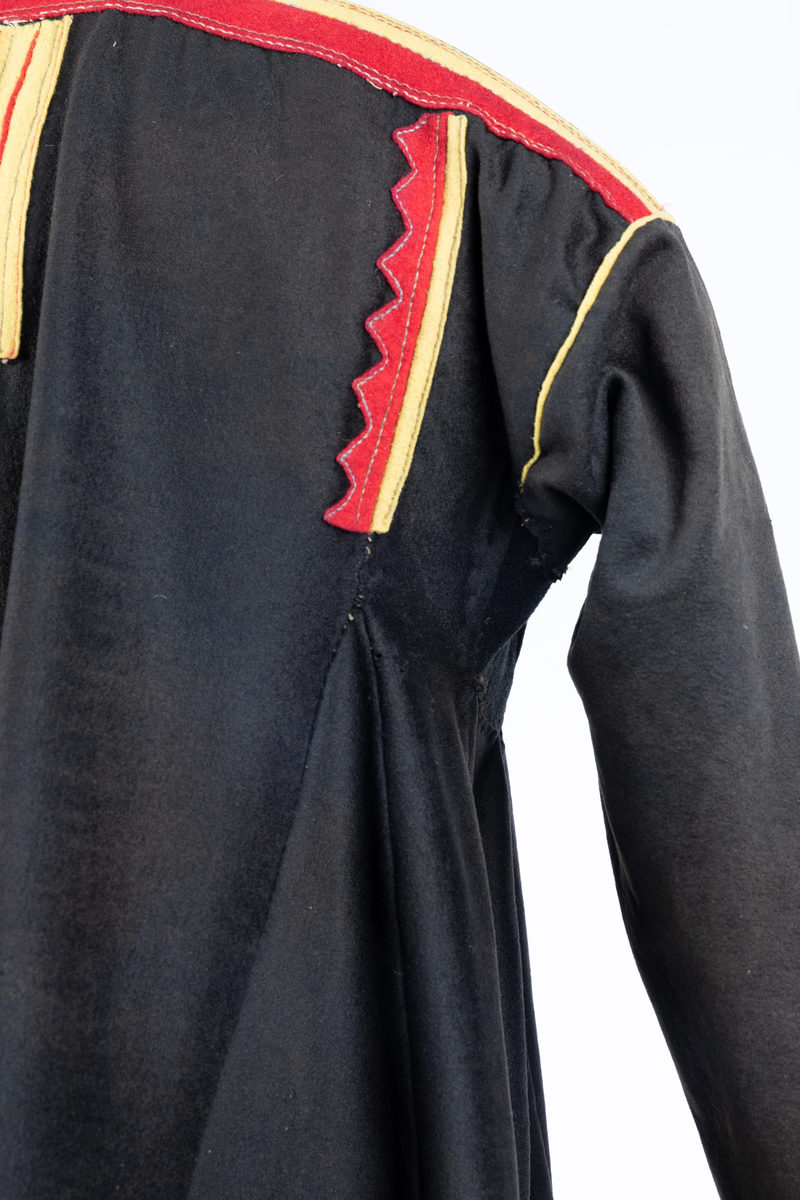 Svart kofte av klede med dekor av gult, rødt og beige klede.