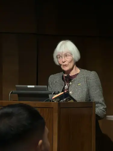 En kvinne med hvitt hår snakker ved en talerstol.