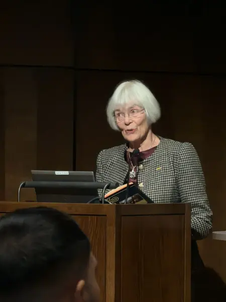 En kvinne med hvitt hår snakker ved en talerstol.