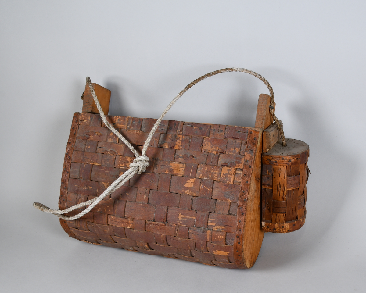 Tegerflettet fiskeveske. Avlang form med avrundet bunn. Sidevegger av tre. Veskestropp av tvinnet tekstil. På siden henger det en tegerflettet markebutt.