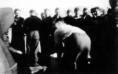 Arbeidsoppgaver ved 7. motorminesveiperflotilje (7. R-Fl). Fototekst: "Einer arbeitet, 20 sehen zu!" ("En jobber mens 20 ser på!").