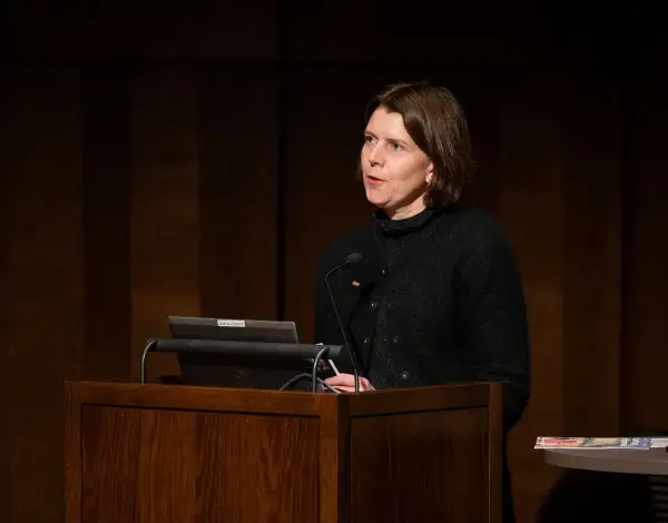 En kvinne med mørkt hår og sorte klær bak en talerstol.