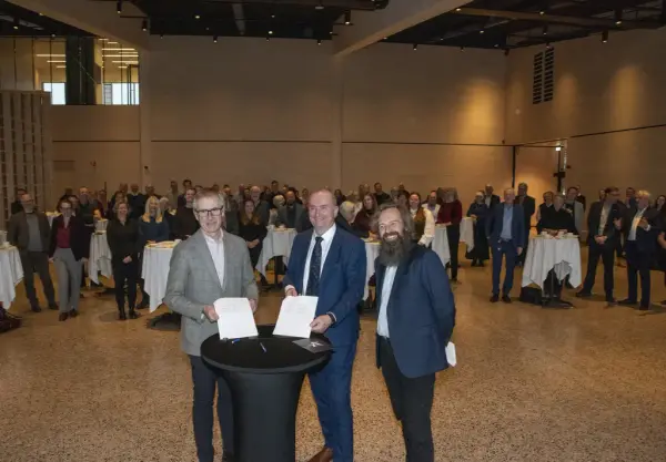 Øystein Nordal hos Martin M. Bakken, Sven Inge Sunde hos Anno museum og Per Øyvind Riise hos Anno Domkirkeodden viser stolt fram den signerte overtakelseskontrakten for Anno Domkirkeodden historiesenter. De rundt 100 inviterte gjestene vises i bakgrunnen.